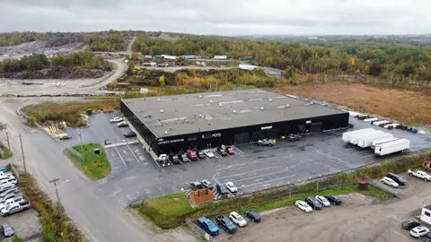 Aerial view of the renewed building in black cladding, with tenant signage, parking and trailers, in autumn