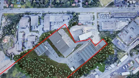 Top-down site plan rendering with the property line outlined in red, showing three industrial buildings with parking and truck courts on a wooded site among existing industrial lots
