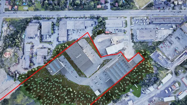 Top-down site plan rendering with the property line outlined in red, showing three industrial buildings with parking and truck courts on a wooded site among existing industrial lots