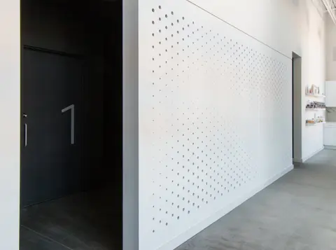 White perforated screen wall along the corridor beside a dark door